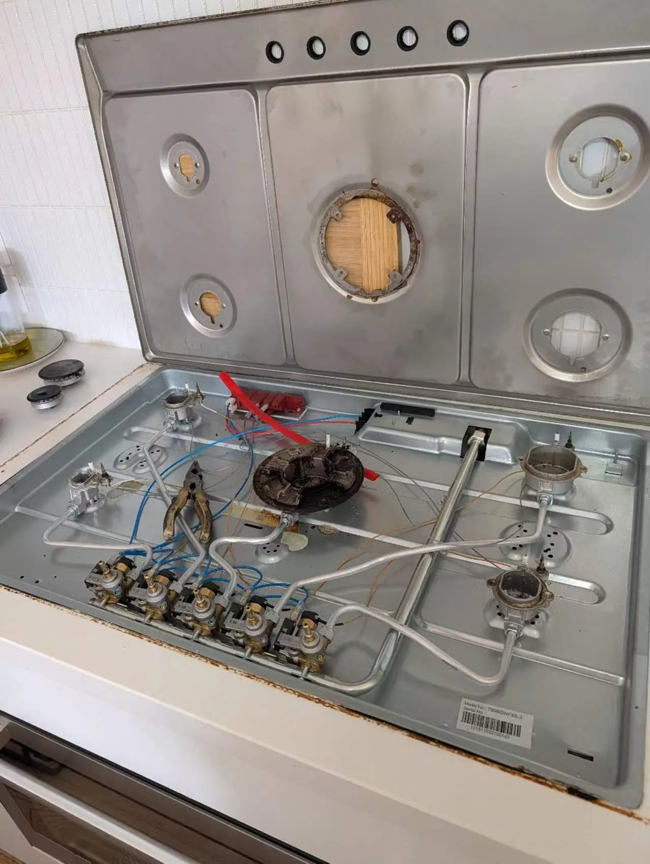 Cooktop lifted to show internal burner and connection components